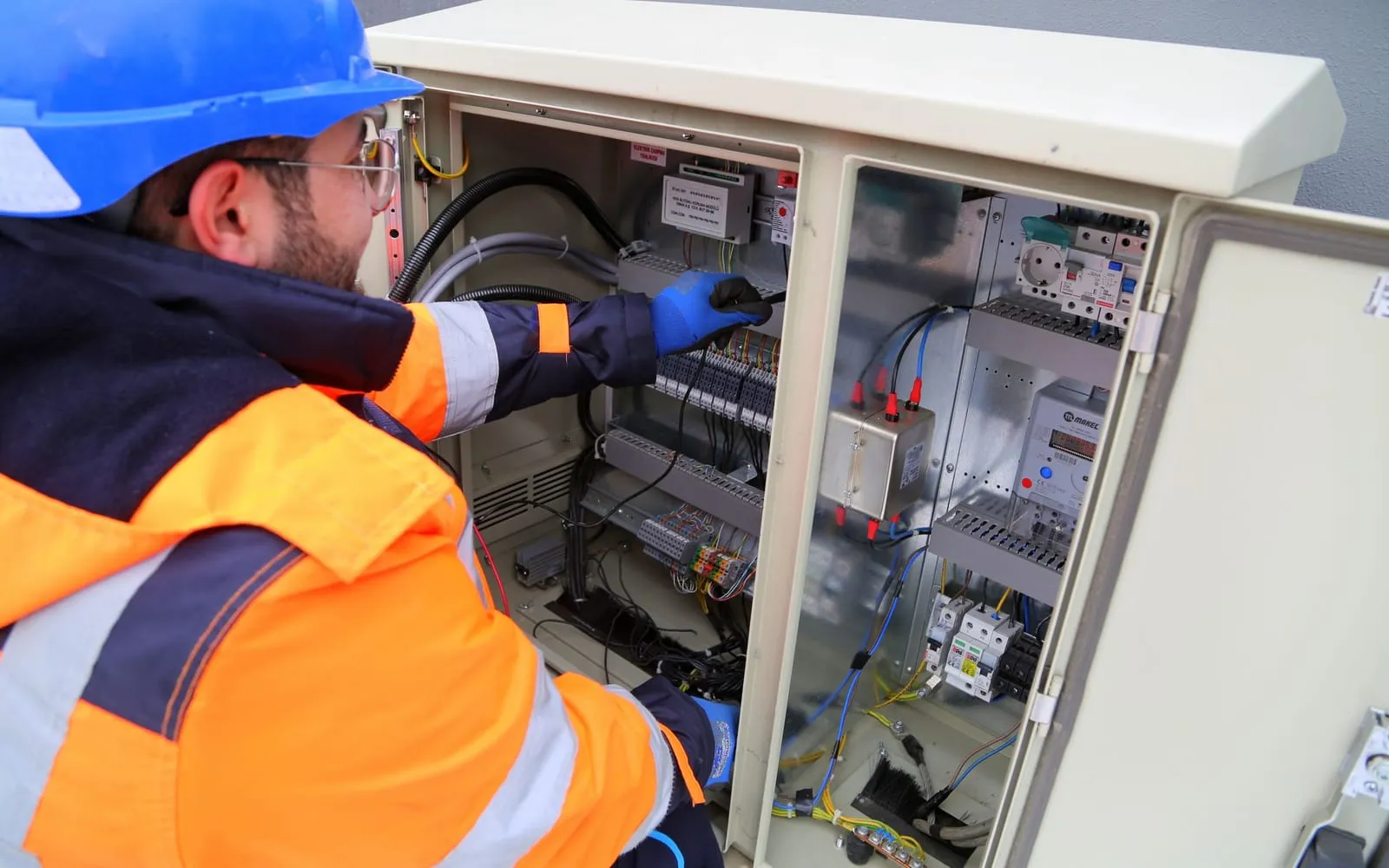 Técnico com capacete trabalhando em painel elétrico de comando